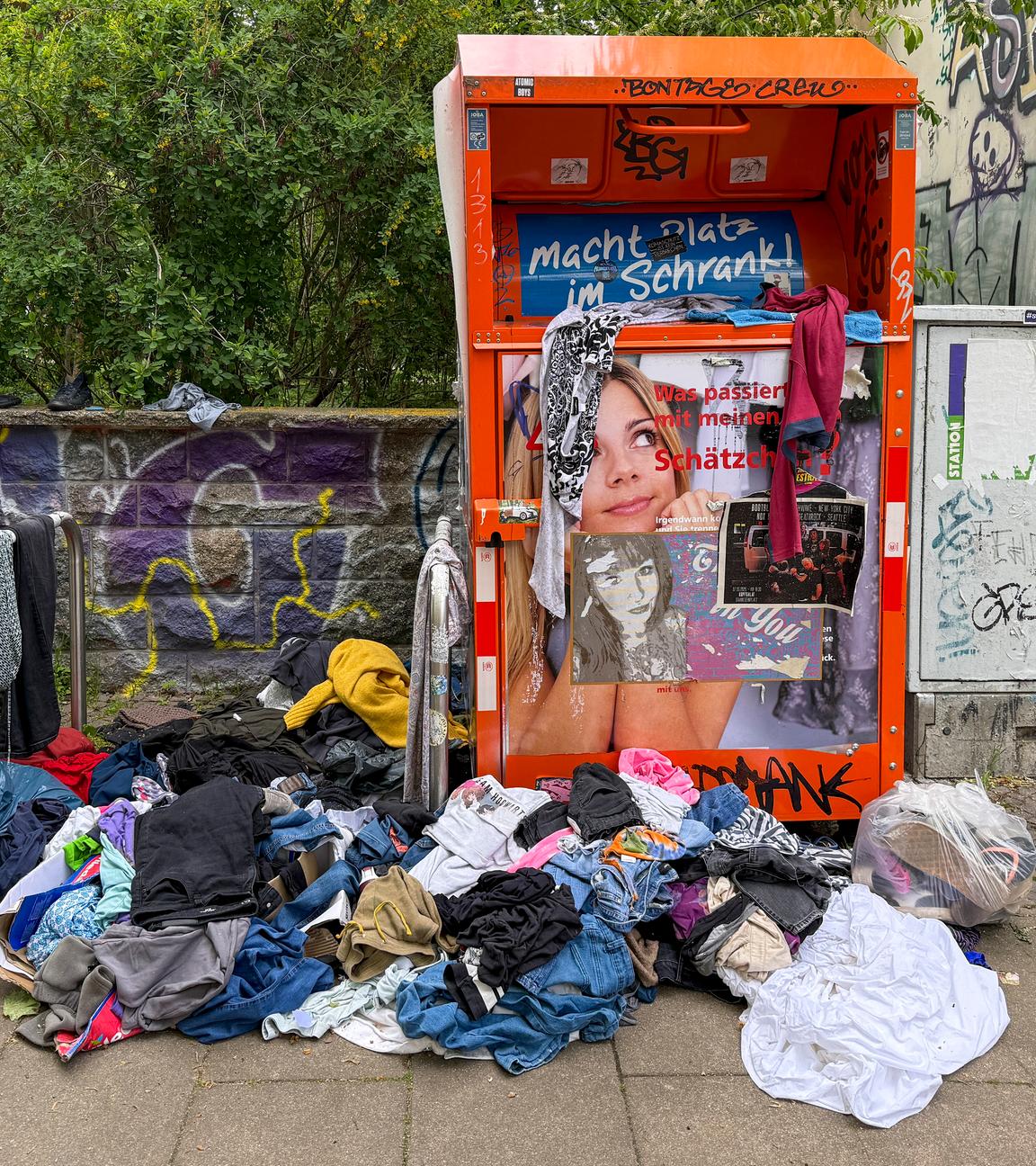 Symbolbild: Aufgerissene Müllsäcke und wild umhergeworfene Kleidung liegen vor einem Altkleidercontainer. 