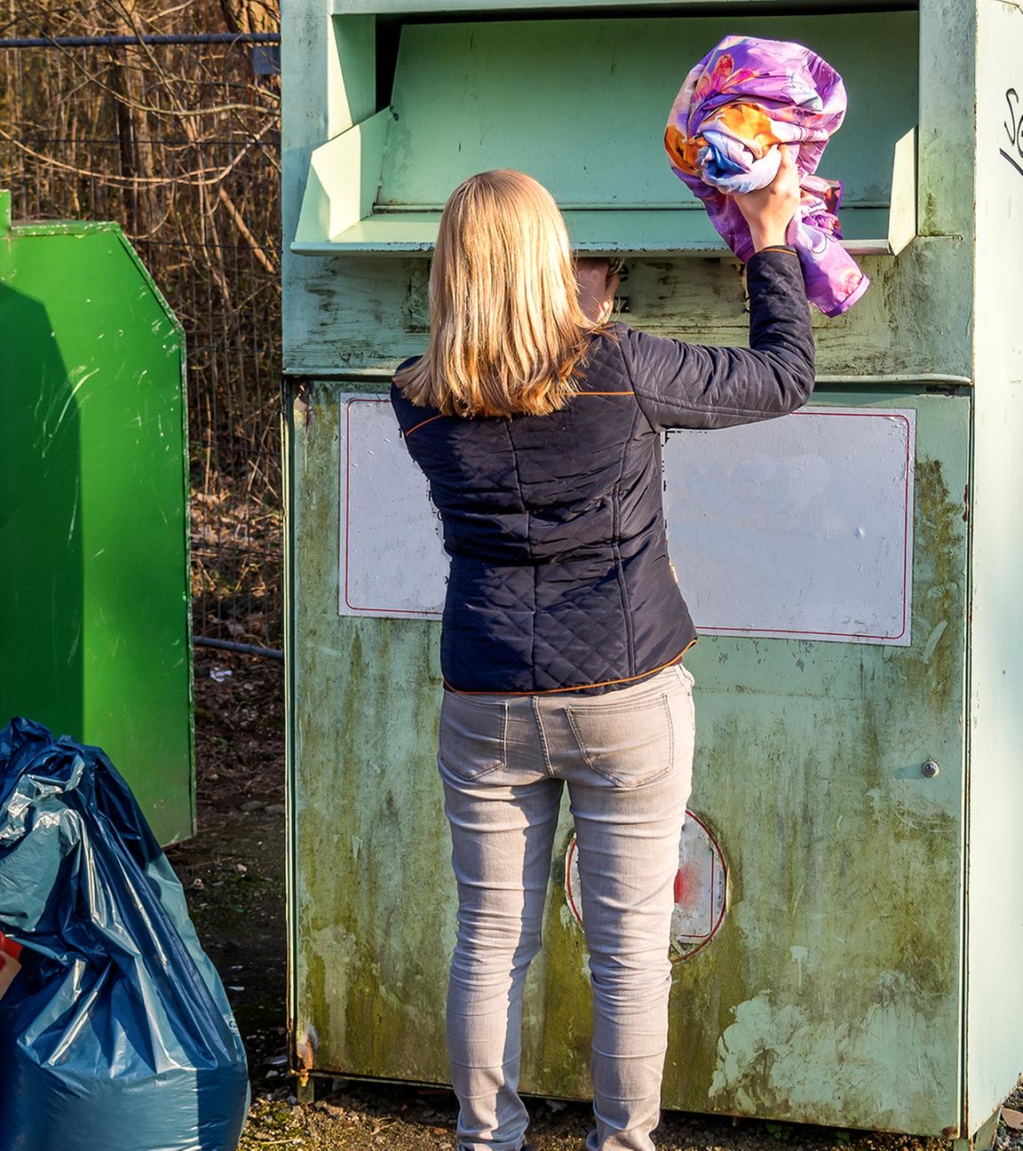 Übervolle Altkleidercontainer und falsche Entsorgung: Frau wirft Kleidung in Altkleidercontainer