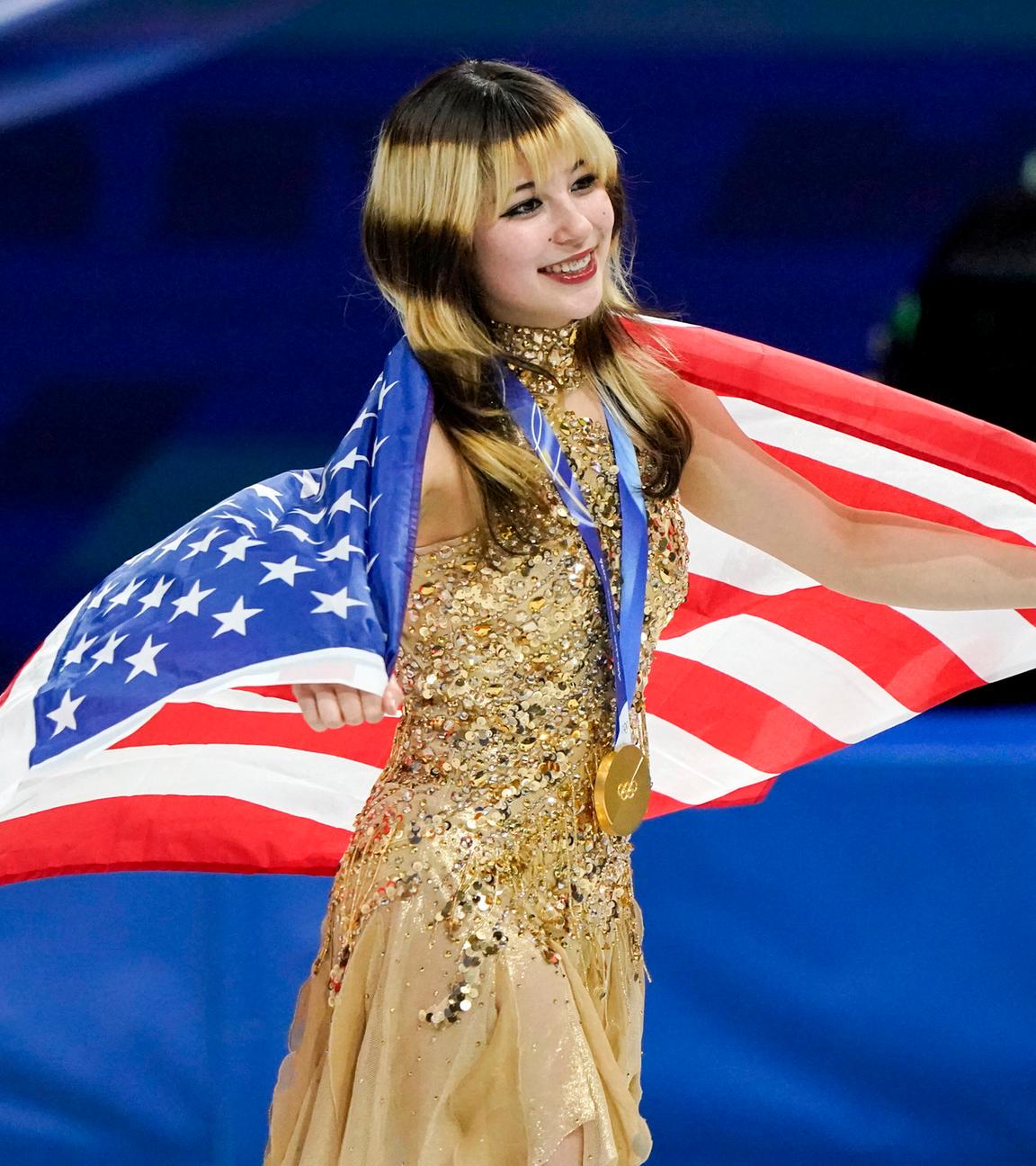 Alysa Liu ist Olympiasiegerin im Eiskunstlauf und präsentiert eingehüllt in der US-amerikanische Flagge ihre Goldmedaille.
