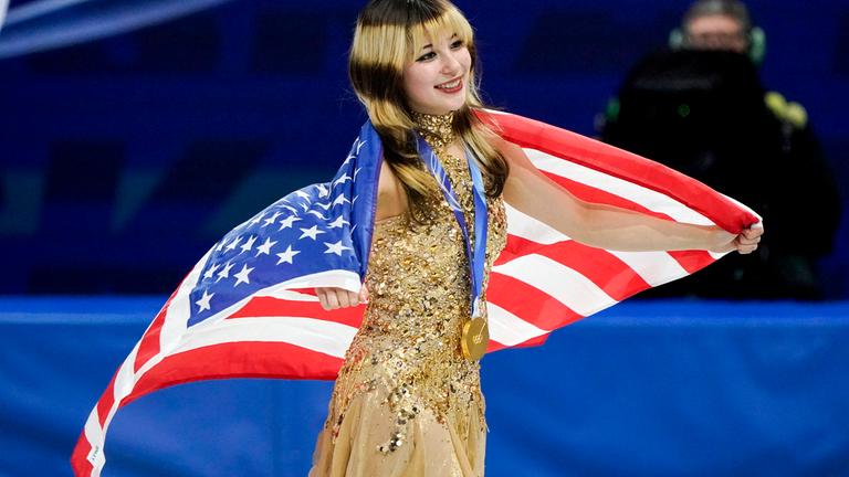 Alysa Liu ist Olympiasiegerin im Eiskunstlauf und präsentiert eingehüllt in der US-amerikanische Flagge ihre Goldmedaille.