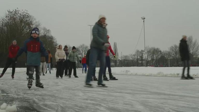 Kinder und Erwachsene laufen mit Schlittschuhen auf einer Eisbahn.
