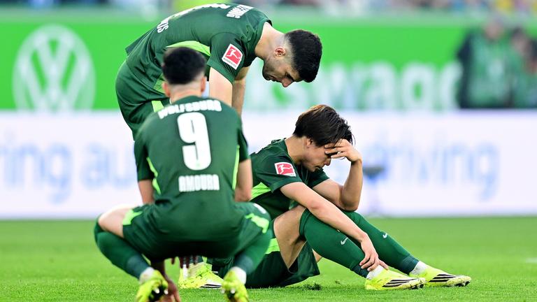 Die Wolfsburger Mohamed Amoura, Konstantinos Koulierakis und Kento Shiogai sitzen ratlos nach der Niederlage gegen den Hamburger SV am Boden
