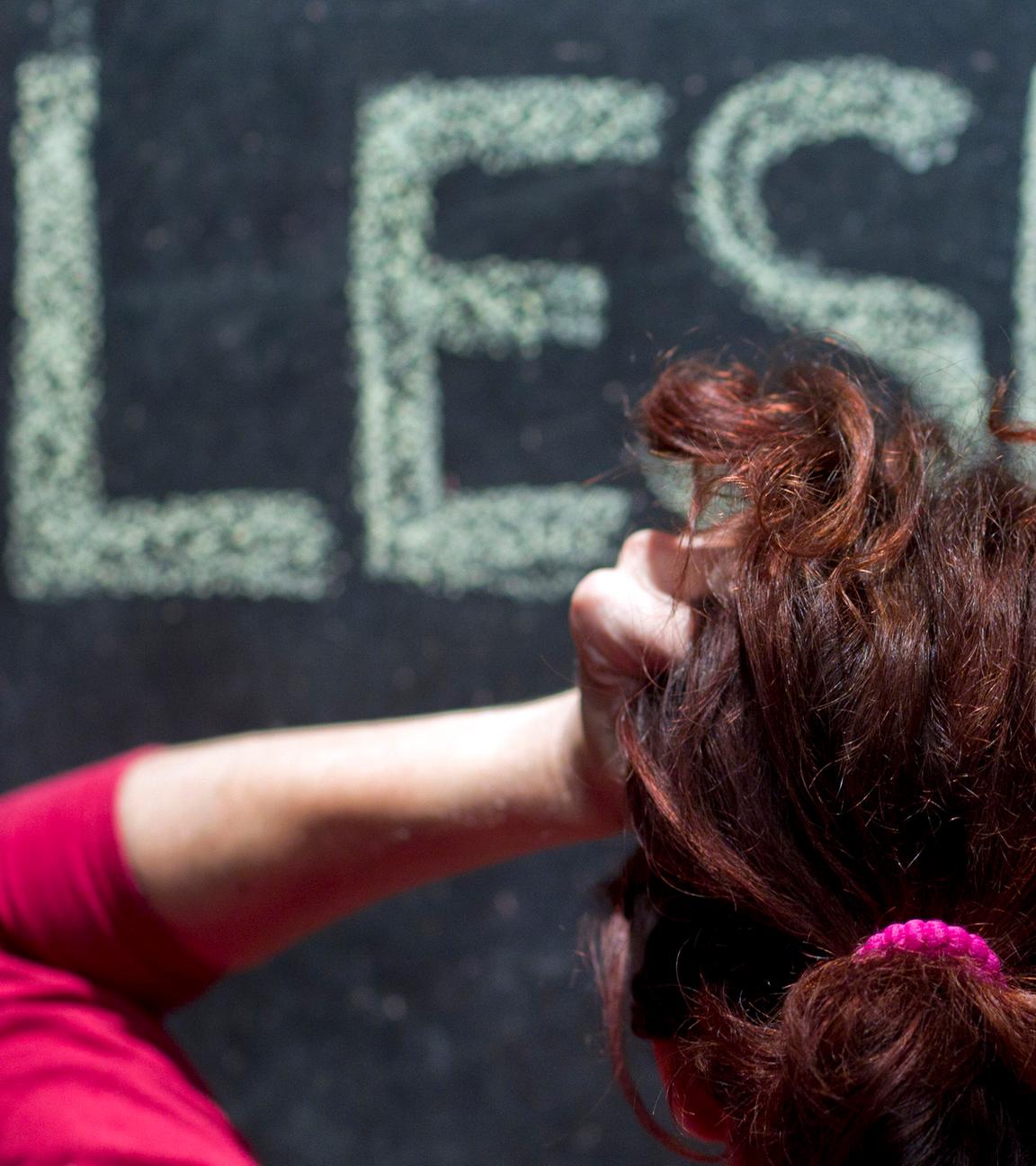 Eine Frau rauft sich vor einer Schultafel mit der Aufschrift "Lesen" die Haare.