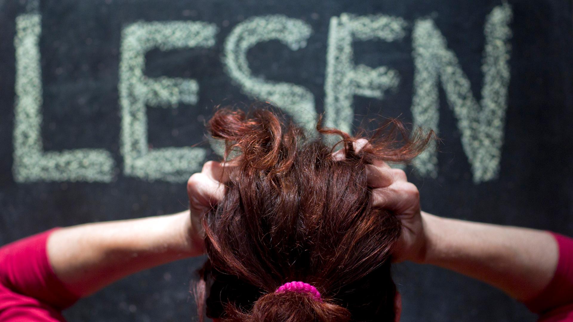 Eine Frau rauft sich vor einer Schultafel mit der Aufschrift "Lesen" die Haare.