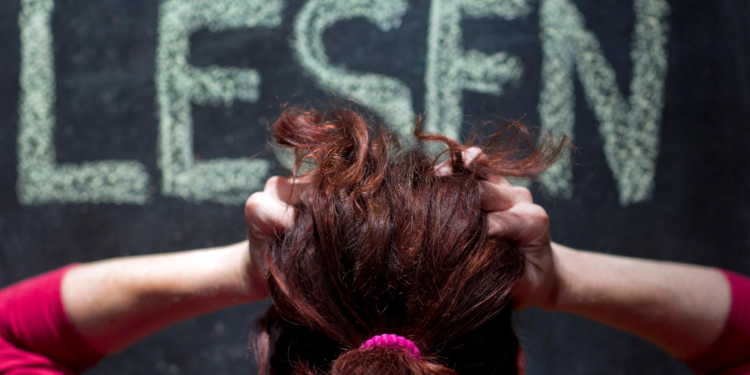 Eine Frau rauft sich vor einer Schultafel mit der Aufschrift "Lesen" die Haare.