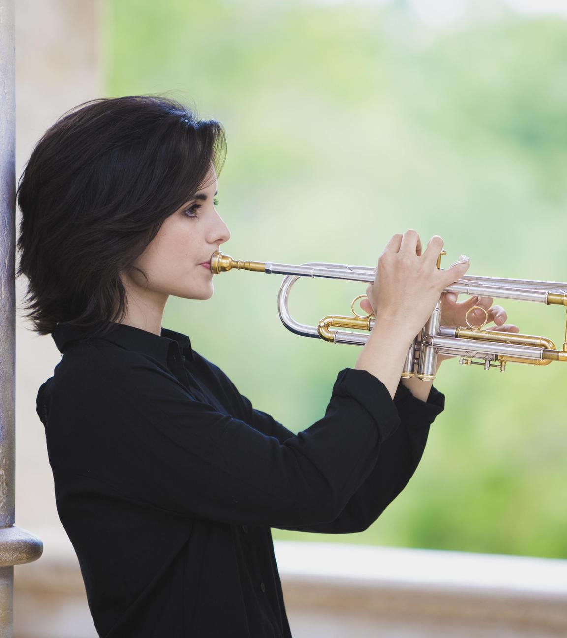 Die junge Trompeterin Andrea Motis in dunklem Pullover, seitlich, die Trompeter angesetzt und waagerecht haltend.