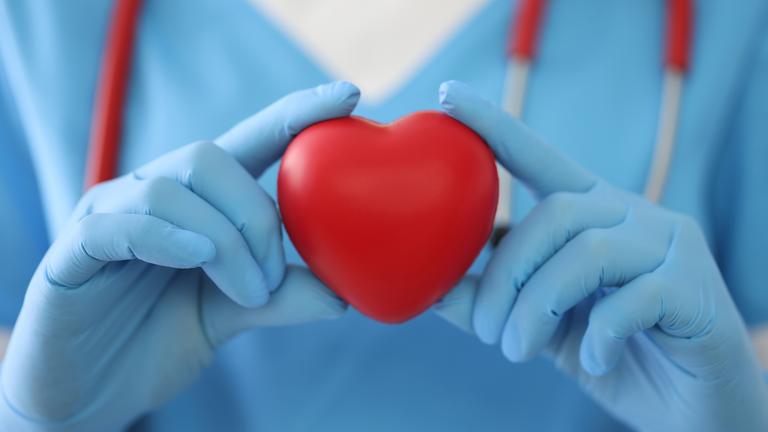 Ein Arzt mit Handschuhen hält ein symbolisches Herz vor der Brust.