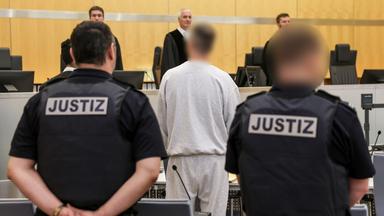 Der Angeklagte (mittig) steht zwischen Justizangestellten im Gerichtssaal Düsseldorf am 04.05.2026 während des Prozesses um Politiker-Todeslisten, die er auf der Darknet-Plattform veröffentlichte.