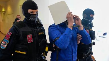 Der Angeklagte verbirgt sein Gesicht hinter Aktenordnern, als er von zwei Beamten der Justizwache aus dem Gerichtssaal des Bezirksgerichts geführt wird.