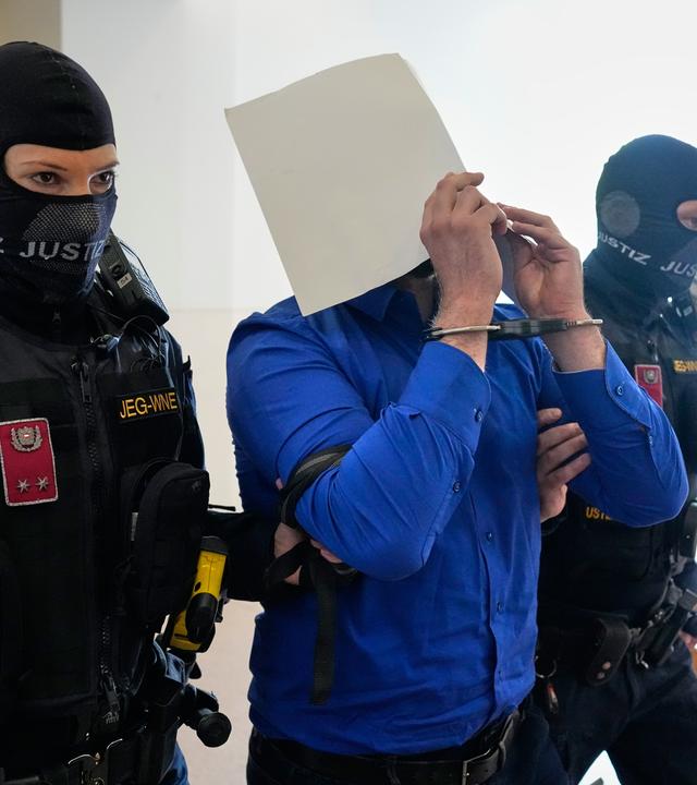 Der Angeklagte verbirgt sein Gesicht hinter Aktenordnern, als er von zwei Beamten der Justizwache aus dem Gerichtssaal des Bezirksgerichts geführt wird.