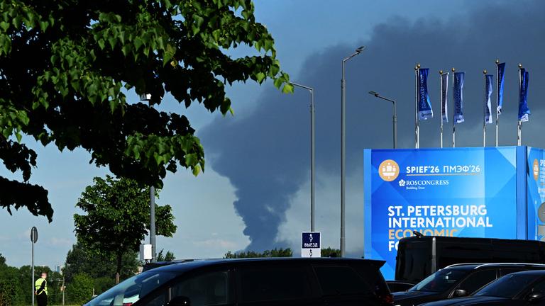 Am 03.06.2026 sind im russischen Sankt Petersburg Autos zu sehen, die in der Nähe von Bannern mit dem Logo des Internationalen Wirtschaftsforums von Sankt Petersburg (SPIEF) am Veranstaltungsort des Forums geparkt sind, während in der Ferne schwarzer Rauch aufsteigt. 