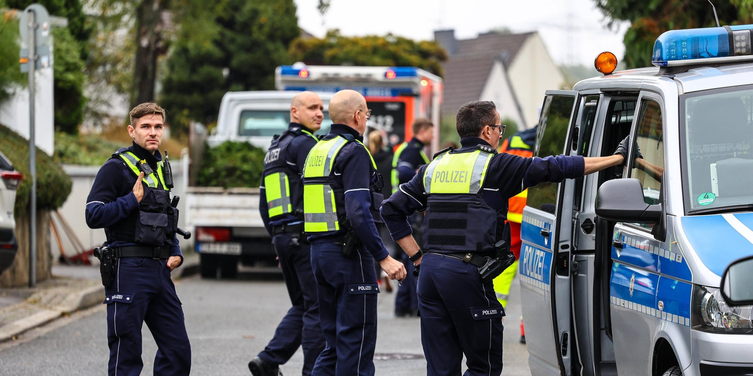 Vier Polizisten bei einem Einsatz neben einem Polizeiauto.