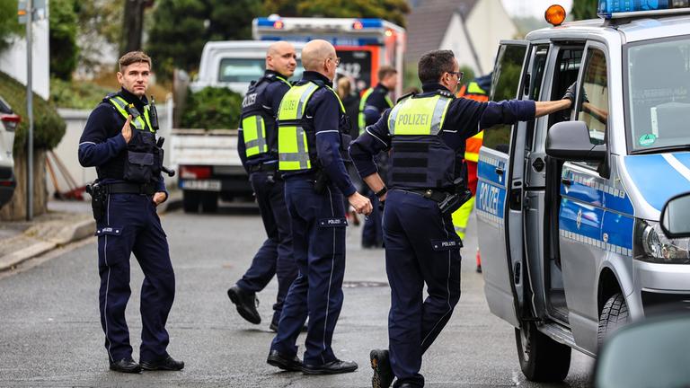 Vier Polizisten bei einem Einsatz neben einem Polizeiauto.