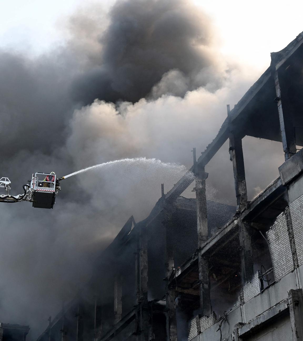 Ukraine, Charkiw: Eine Einsatzkraft der Feuerwehr löscht von einer Plattform aus ein Feuer an einem Gebäude, nachdem es durch russische Luftangriffe beschädigt wurde.
