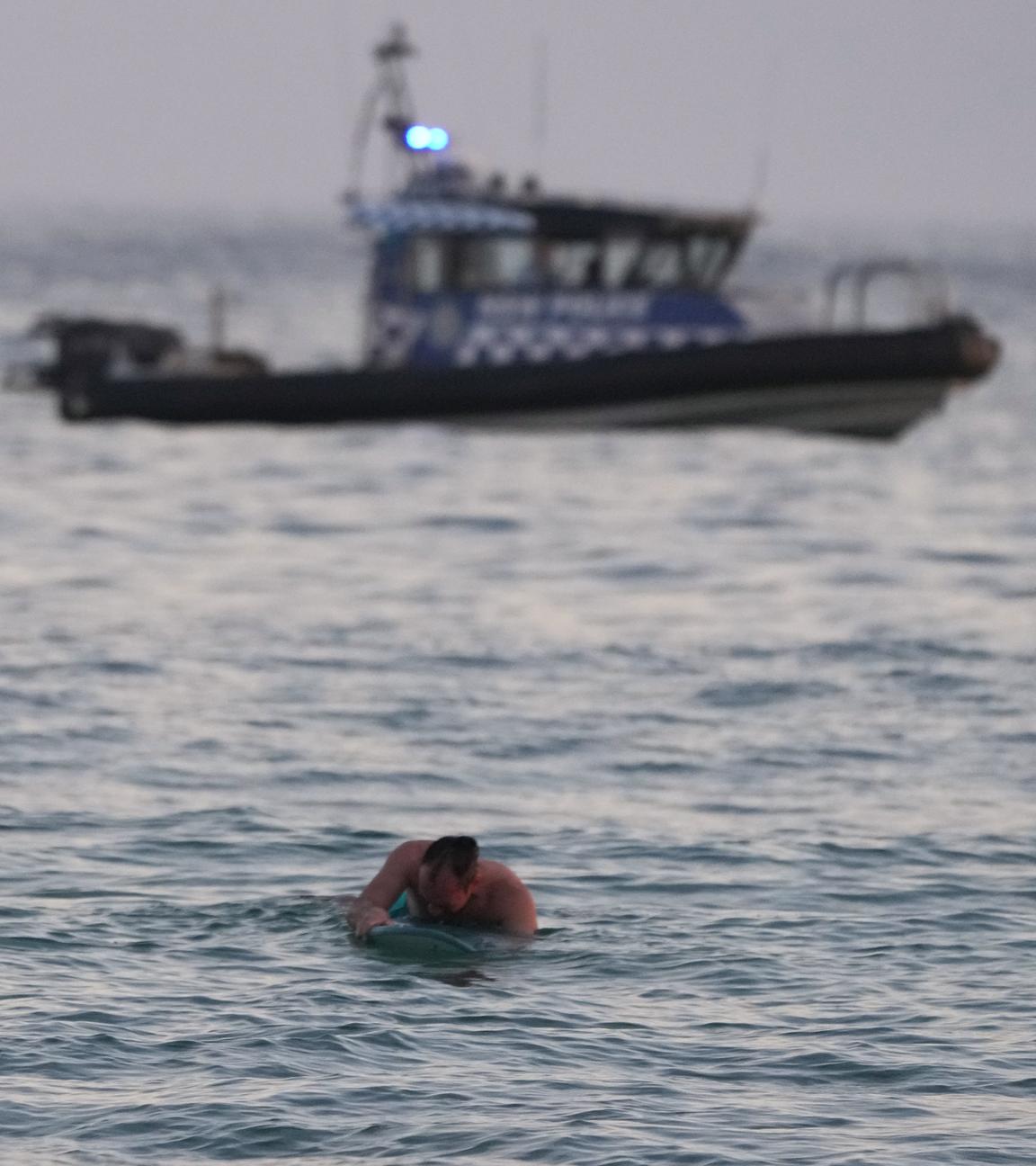 Ein Surfer paddelt zurück ans Ufer, während ein Polizeiboot nach einem Zwischenfall am Bondi Beach in Sydney auf dem Wasser patrouilliert.