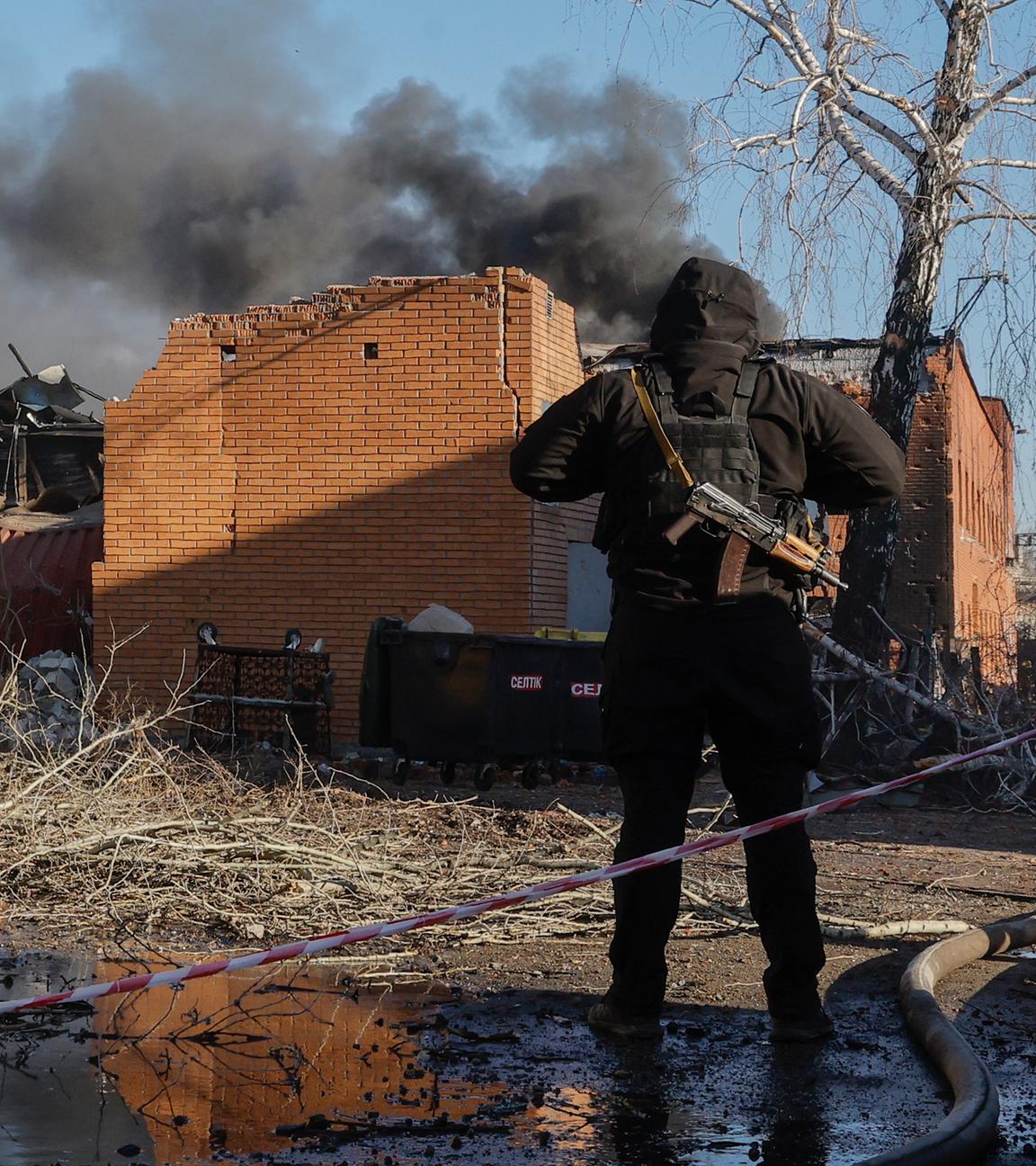 Eine Person sichert ein brennendes Haus im ukrainischen Kriegsgebiet