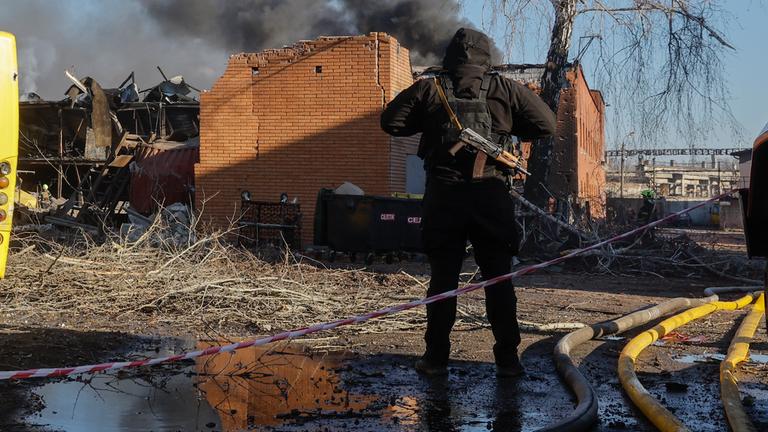 Eine Person sichert ein brennendes Haus im ukrainischen Kriegsgebiet