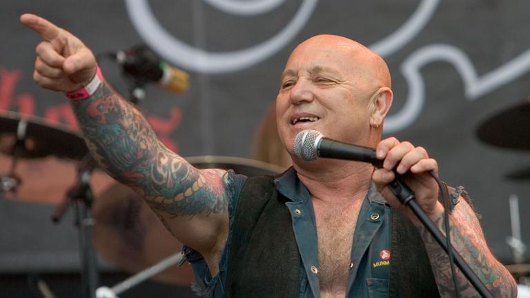 Sänger Angry Anderson steht auf der Bühne und singt.