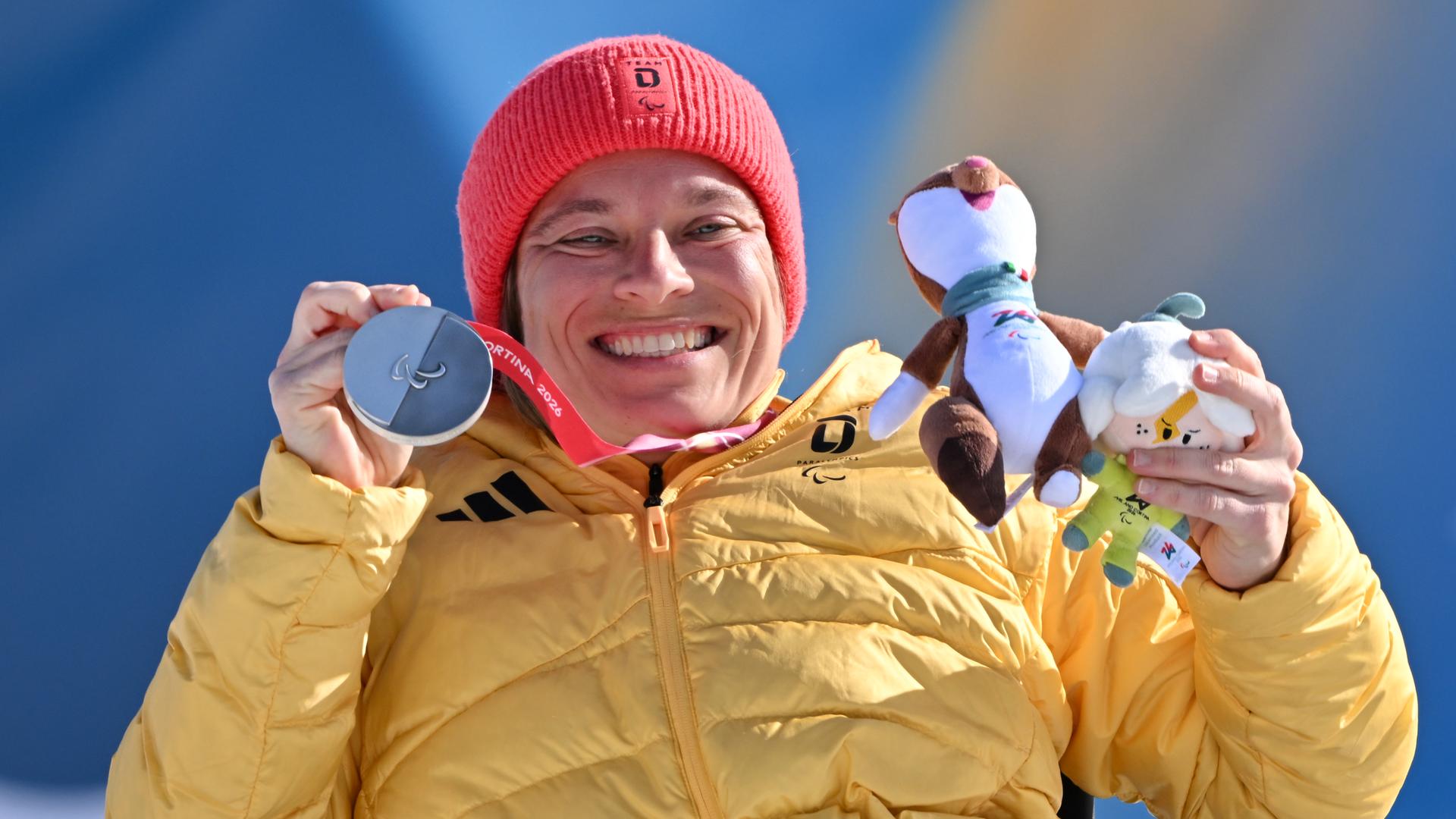 Anja Wicker zeigt ihre Silbermedaille und das Maskottchen der Paralympics lachend in die Kamera.