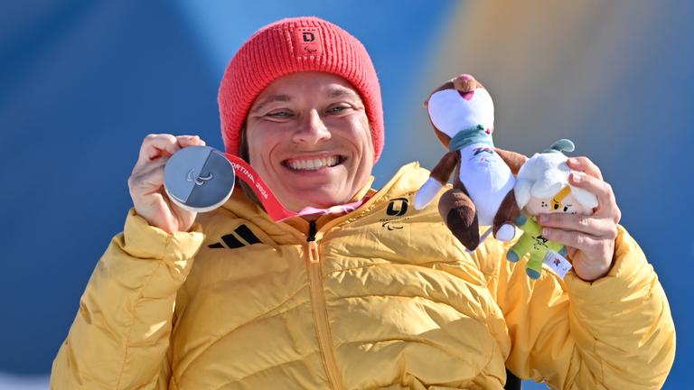 Anja Wicker zeigt ihre Silbermedaille und das Maskottchen der Paralympics lachend in die Kamera.