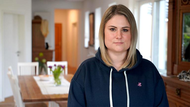 Junge blonde Frau schaut nachdenklich in die Kamera.