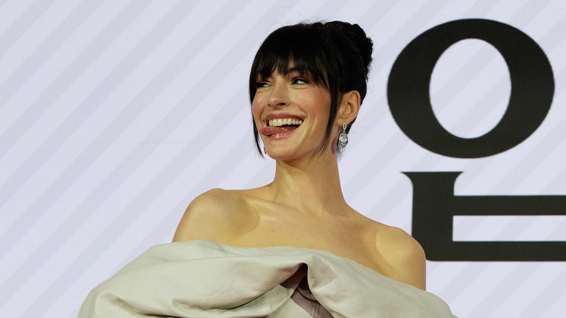 Anne Hathaway steht vor einer Reklamewand