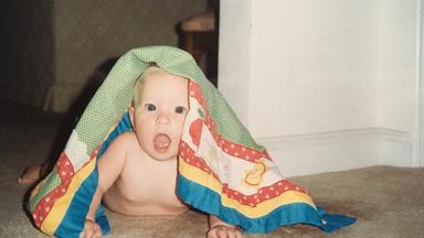 Ein Baby krabbelt auf dem Boden unter einer Decke hervor.