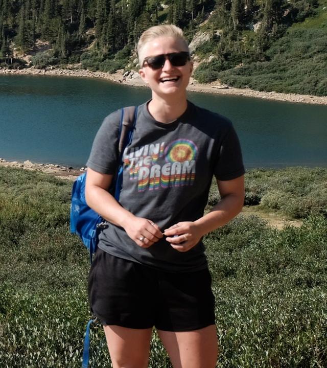 Anne McCarthy steht nach einer Wanderung vor einem See und lächelt in die Kamera.