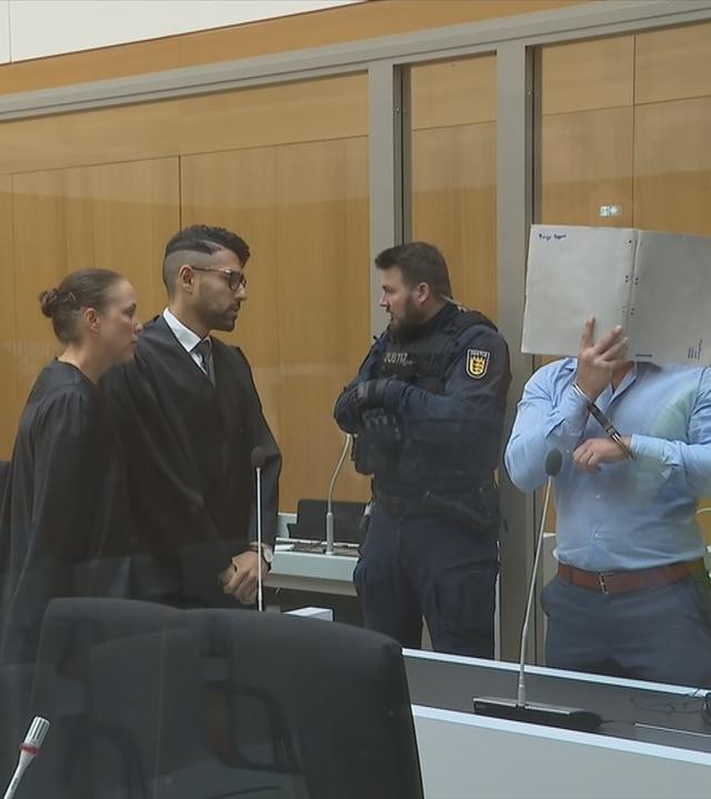 Angeklagter neben Anwälten und Polizisten.