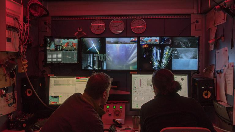 In einem Kontrollraum sitzen Menschen vor Bildschirmen und überwachen die Bohrung in der Tiefe der Antarktis