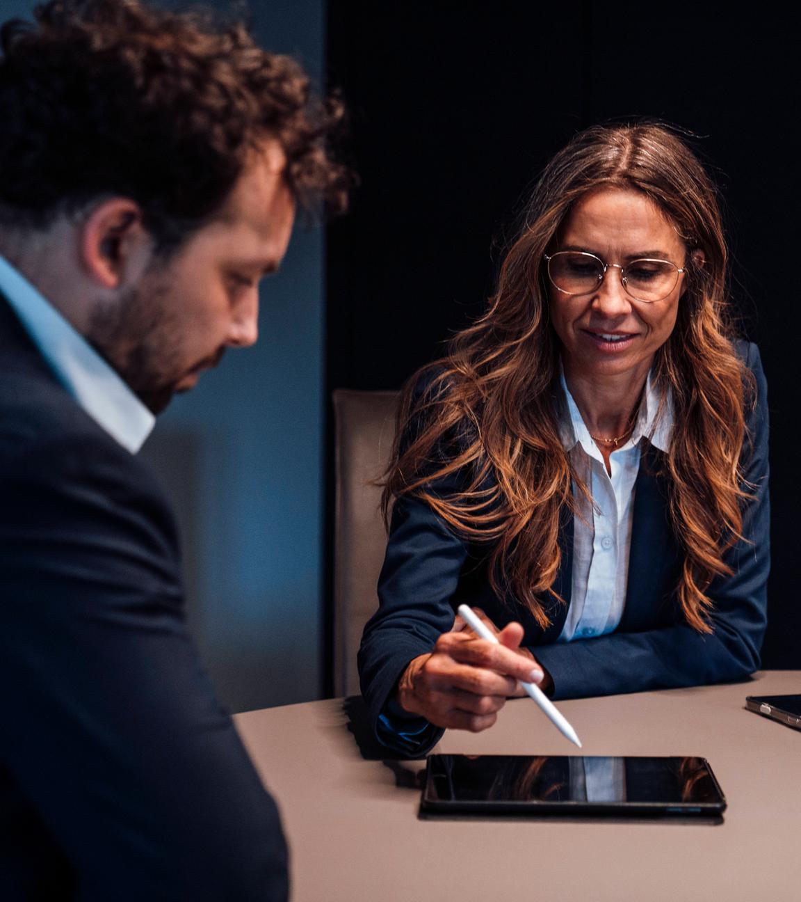 Eine Geschäftsfrau zeigt einem Kollegen in einem Büroraum etwas auf dem Tablet..
