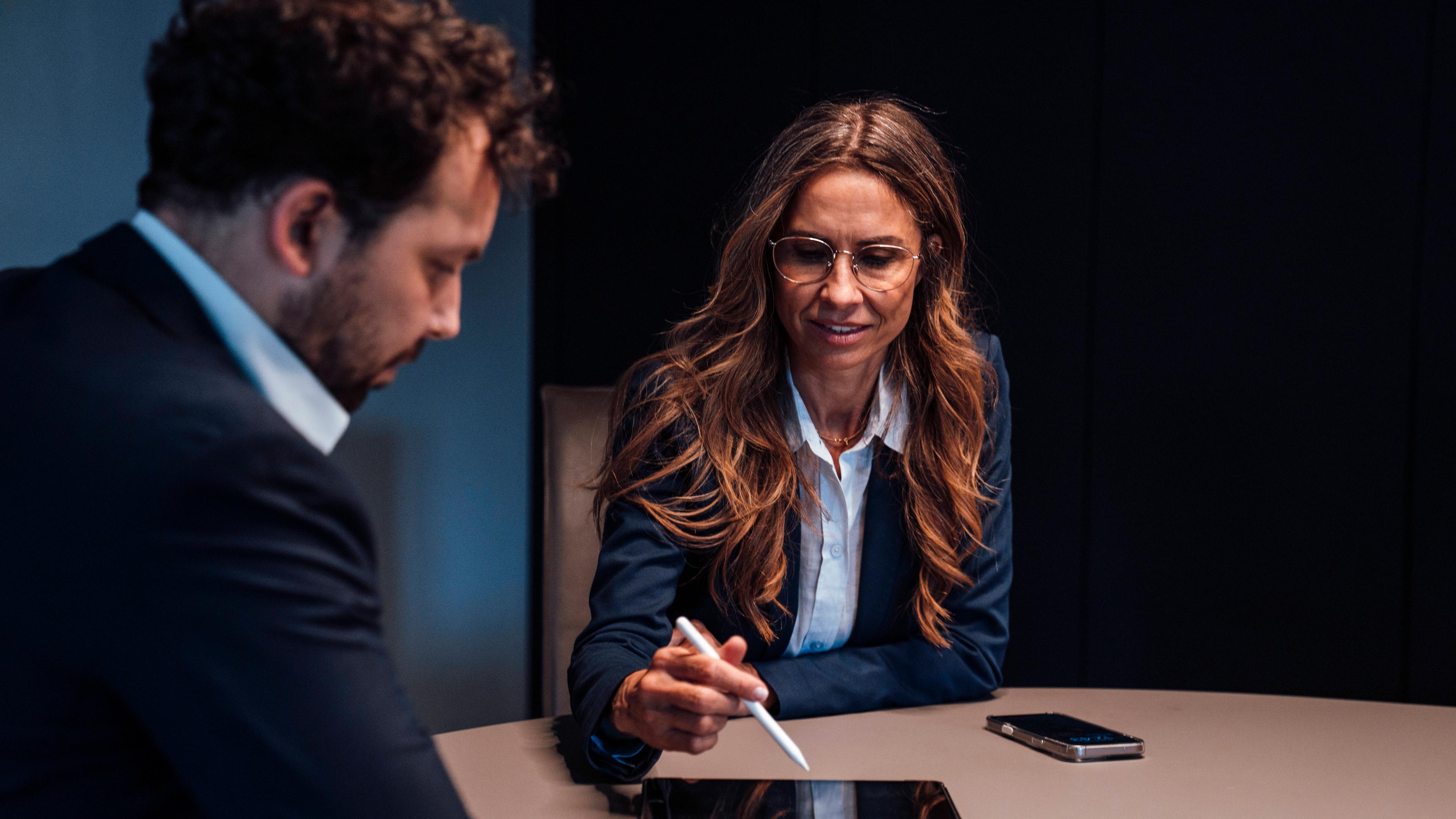 Eine Geschäftsfrau zeigt einem Kollegen in einem Büroraum etwas auf dem Tablet..