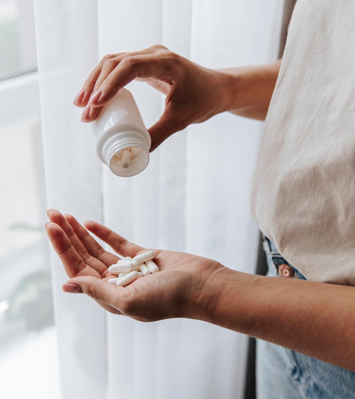 Eine Frau nimmt Tabletten aus einer Medikamentenflasche.
