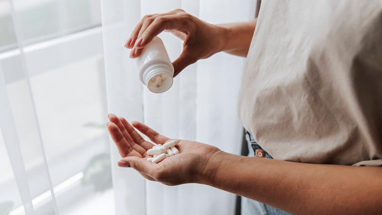 Eine Frau nimmt Tabletten aus einer Medikamentenflasche.