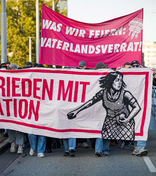 Menschen nehmen in Bremen an einer Demonstration der "Basisgruppe Antifaschismus Bremen" gegen den Tag der Deutschen Einheit teil. Auf Bannern sind die Schriftzüge "Was wir feiern: Vaterlandsverrat!" und "Kein Frieden mit der Nation" zu lesen. 