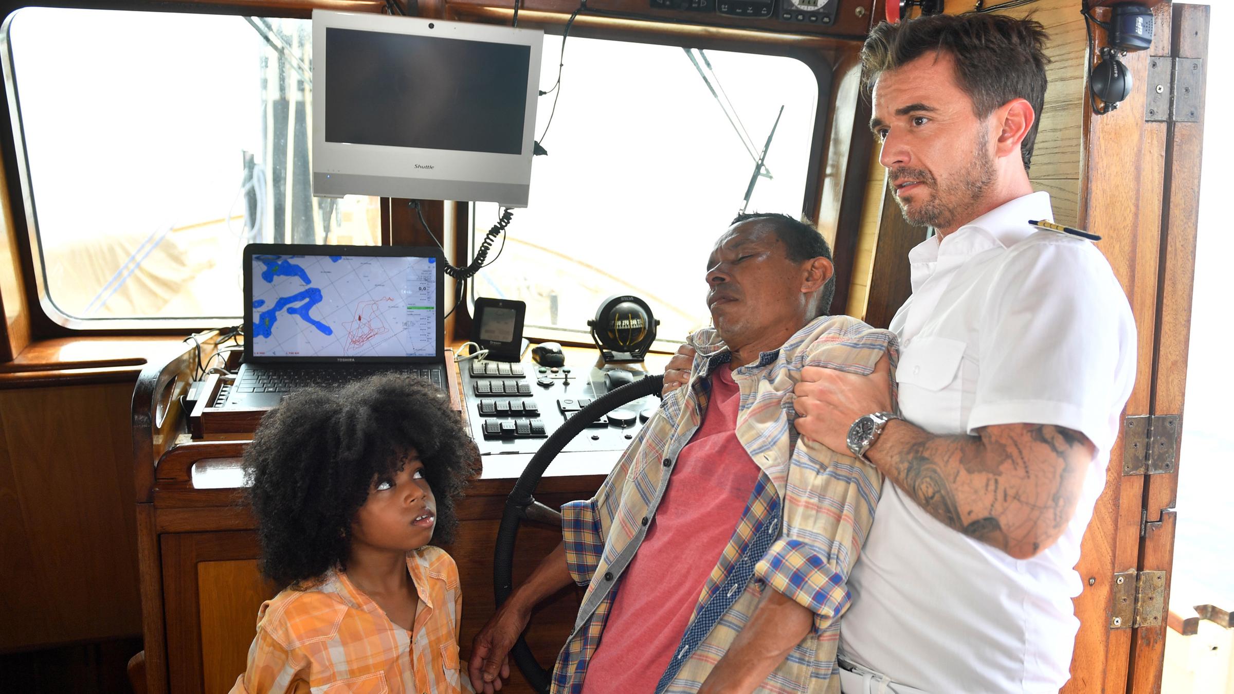 Der kleine Juan (Jordi Ortega) schaut besorgt zu Kapitän Max Pager (Florian Silbereisen), der den bewusstlosen Hernan (Carlos Cardoze) im Arm hält. 