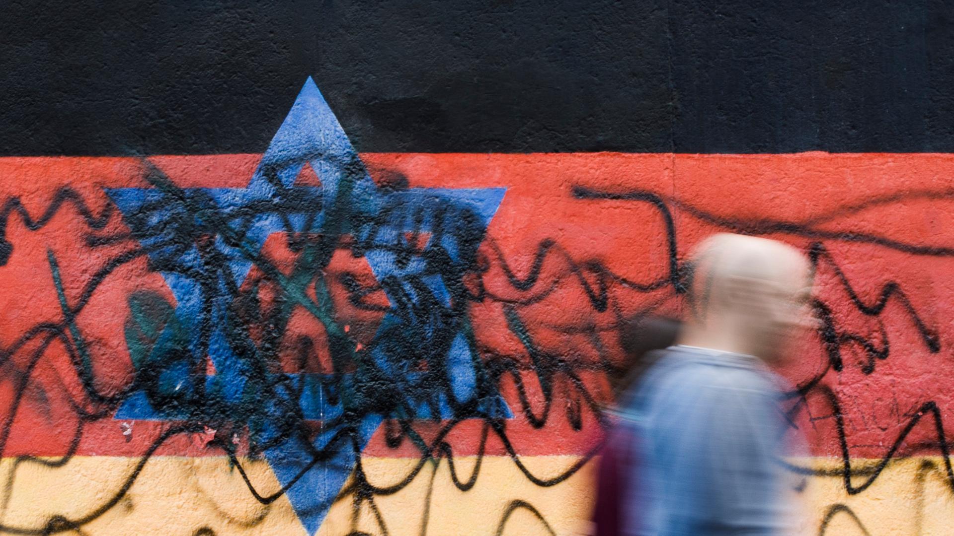 Archiv:  Passanten gehen an dem zerstörten Wandbild des Künstlers Günther Schäfer an der East Side Gallery vorbei. Das Wandbild «Vaterland», das die schwarz-rot-goldene Deutschlandfahne mit einem blauem Davidstern zeigt, wurde von Unbekannten mit schwarzen Graffitis beschmiert