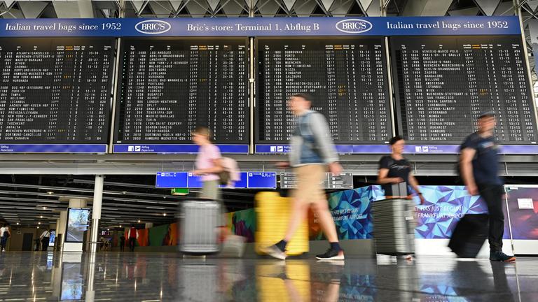Urlauber laufen im Terminal 1 des Frankfurter Flughafens an einer großen Anzeigetafel vorbei.