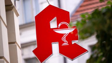 Ein Schild mit dem Apotheken-Logo hängt über dem Eingang zu einer Apotheke in der Innenstadt.