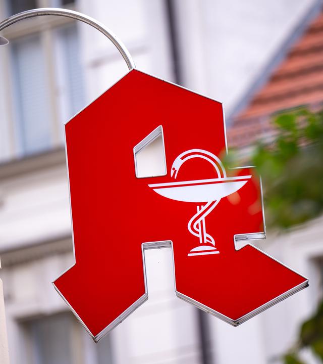 Ein Schild mit dem Apotheken-Logo hängt über dem Eingang zu einer Apotheke in der Innenstadt.