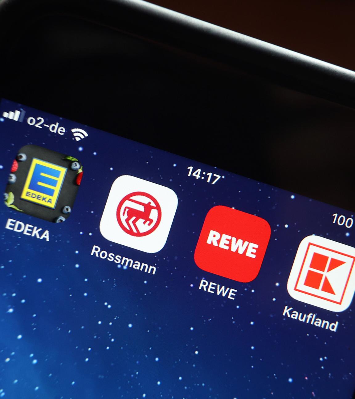 Icons der Apps von den Handelsketten Edeka (l-r), Rossmann, REWE und Kaufland sind auf dem Display eines iPhones zu sehen.