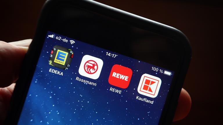 Icons der Apps von den Handelsketten Edeka (l-r), Rossmann, REWE und Kaufland sind auf dem Display eines iPhones zu sehen.