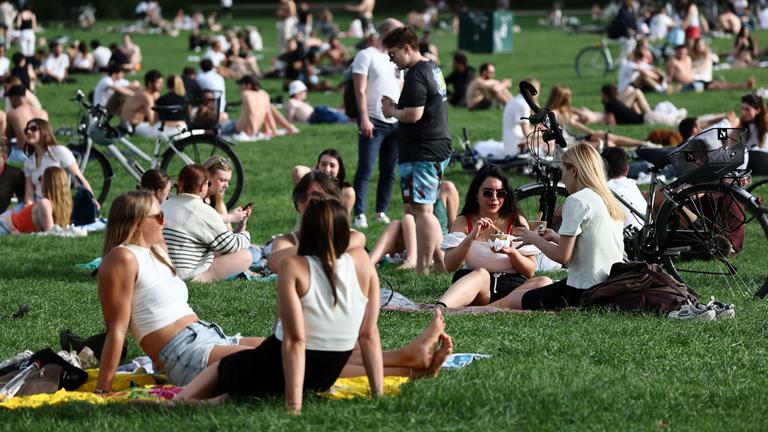 Viele Menschen sitzen bei warmem April-Wetter im Englischen Garten in München