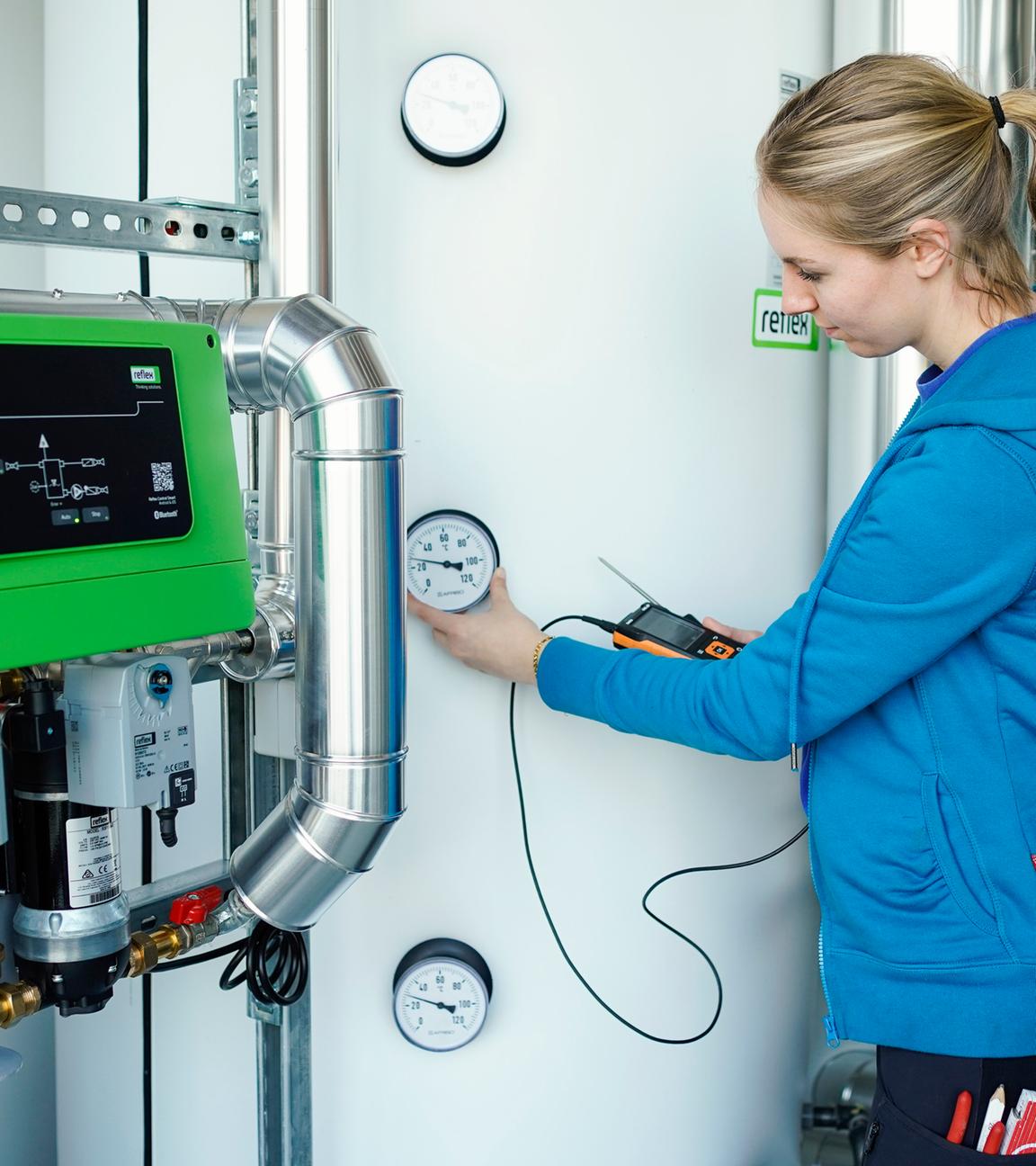 Eine Auszubildene steht vor dem Wärmespeicher einer Wärmepumpe.