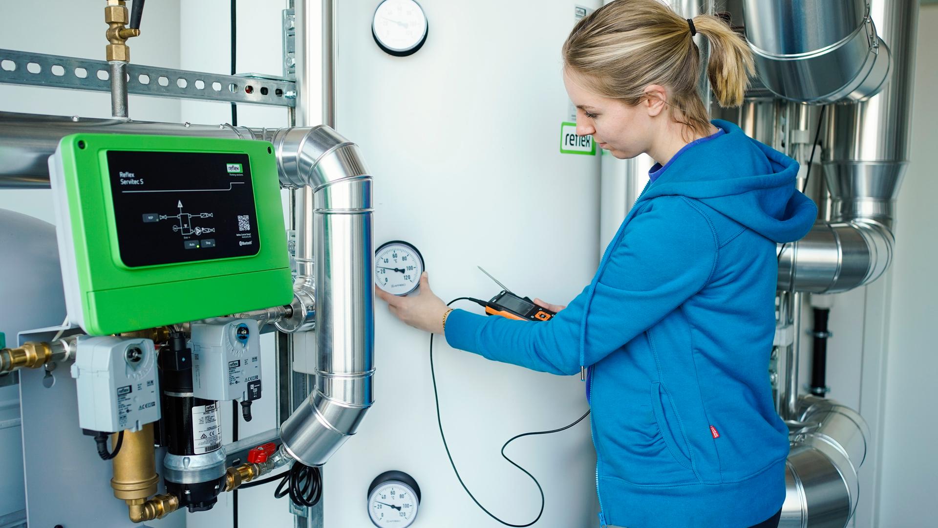 Eine Auszubildende steht vor dem Wärmespeicher einer Wärmepumpe.