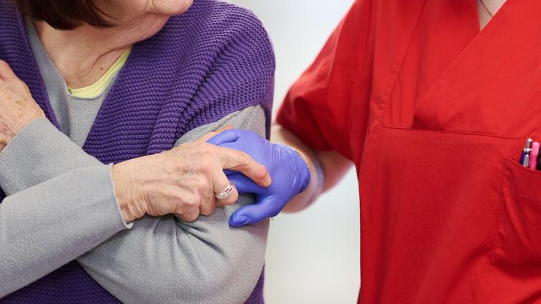 Eine Pflegekraft mit blauen medizinischen Handschuhen nimmt im DRK-Pflegezentrum Solferino eine Bewohnerin an der Hand.