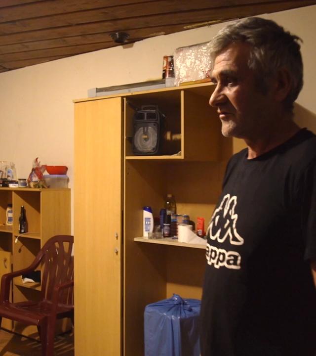 Männliche Arbeitskraft aus Serbien in heruntergekommener Unterkunft bei schummrigem Licht vor Etagenbett und alter Schrankwand