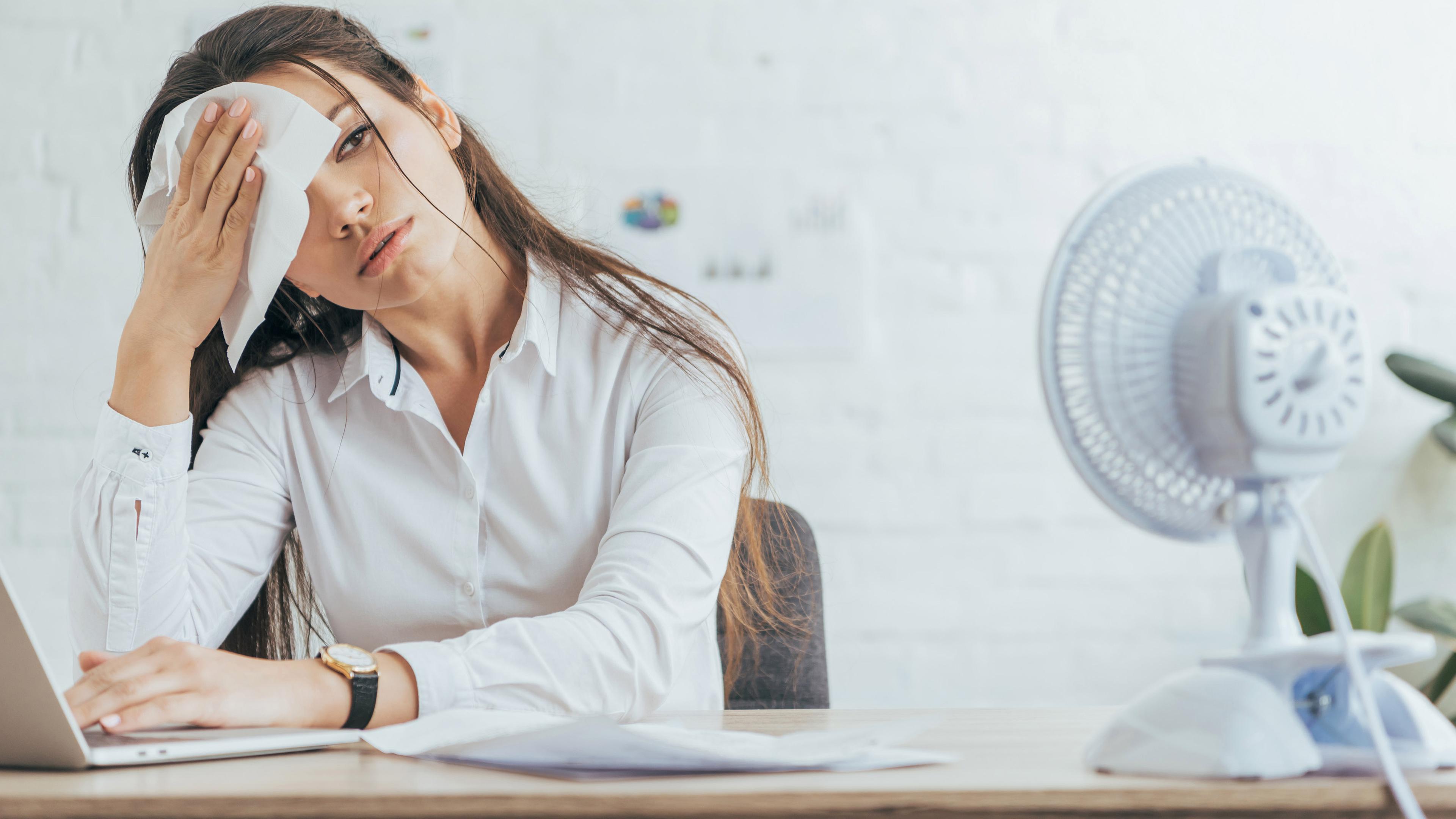 Eine Frau sitzt schwitzend am Arbeitsplatz (Symbolfoto)