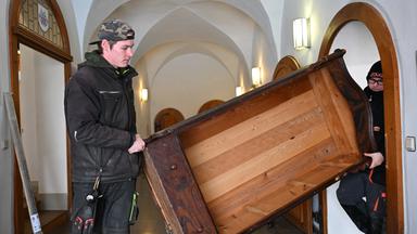 Zwei junge Männer tragen ein aus Holz bestehendes Möbelstück.