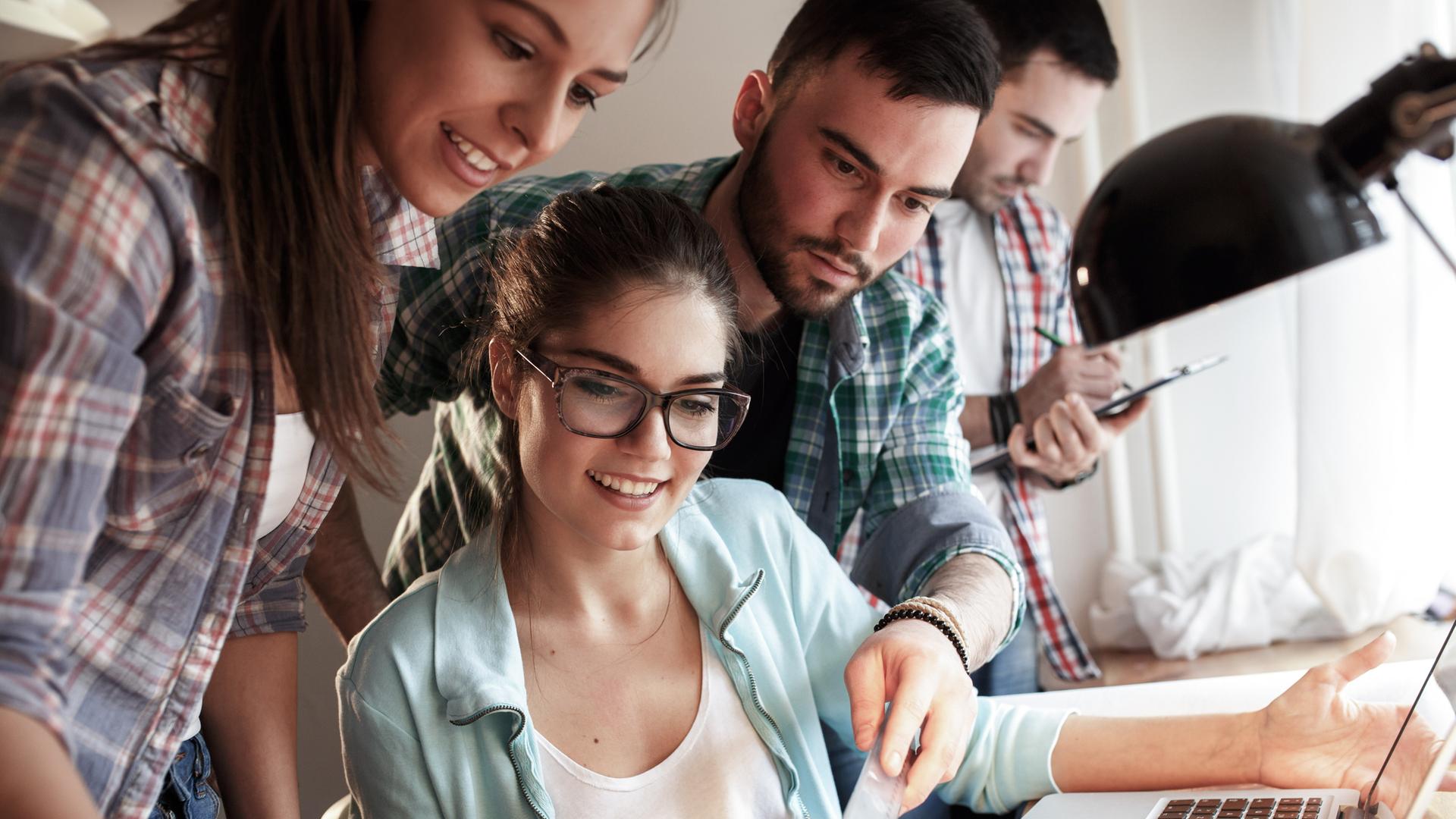 Vier junge Menschen beugen sich bei der Arbeit über einen Schreibtisch.
